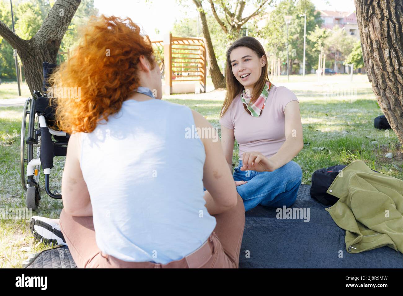 Disabled female person sitting with her friend in a park and having a ...