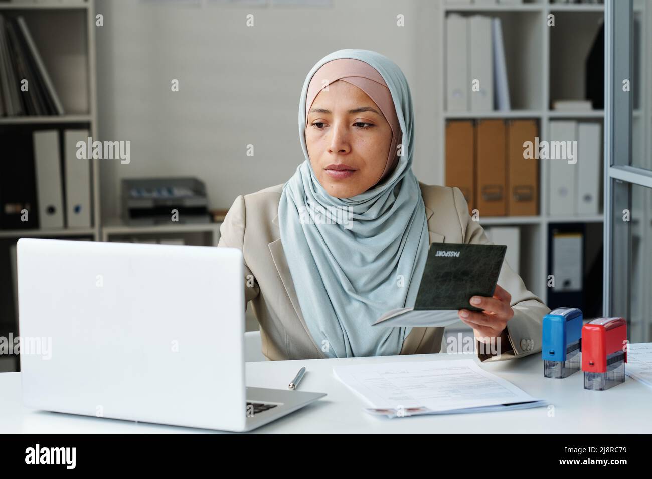 Young adult Muslim woman wearing hijab sitting at desk in embassy ...