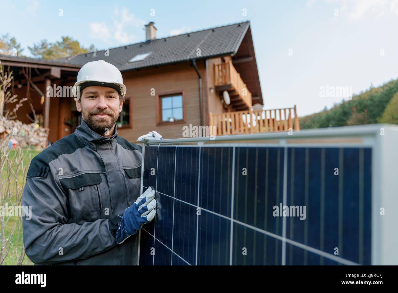 Smiling handyman solar installer carrying solar module while installing solar panel system on house. Stock Photo
