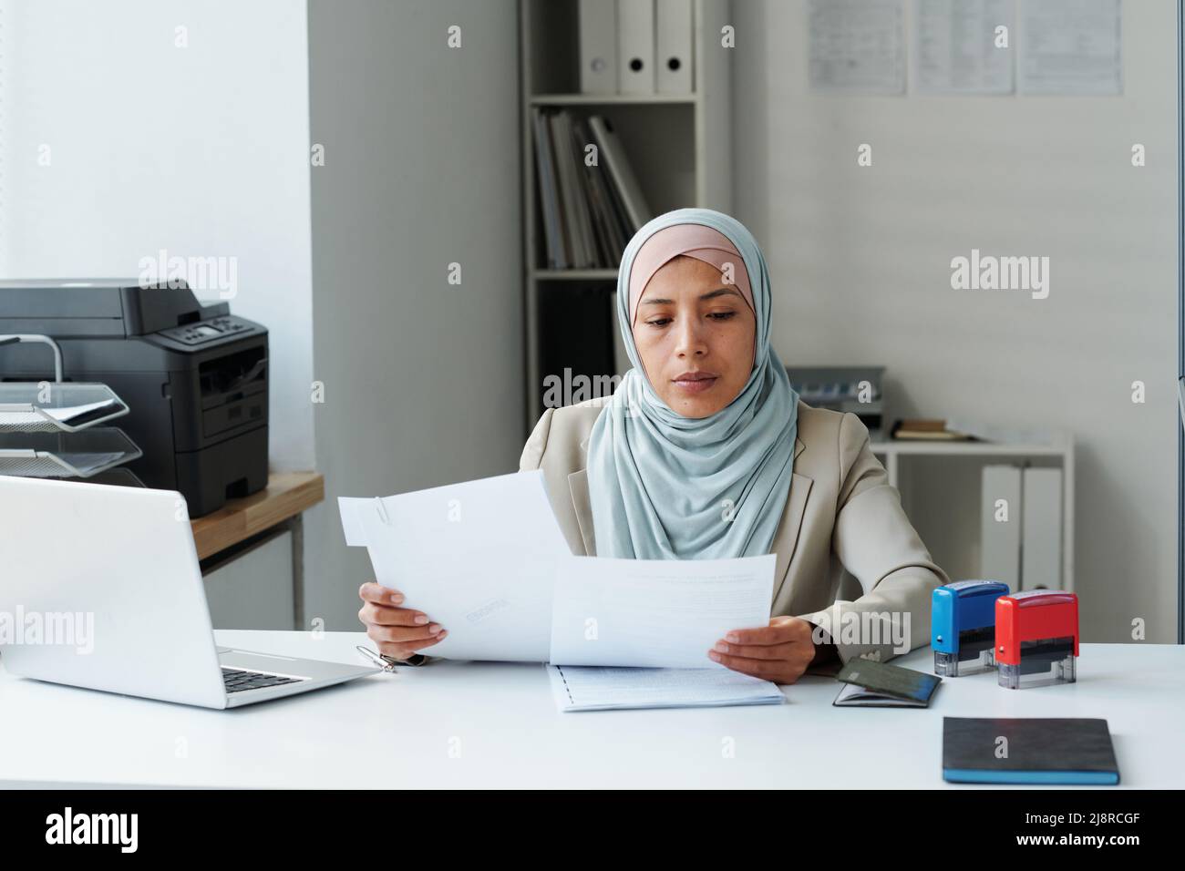 Modern Muslim woman wearing hijab sitting at desk in office doing ...