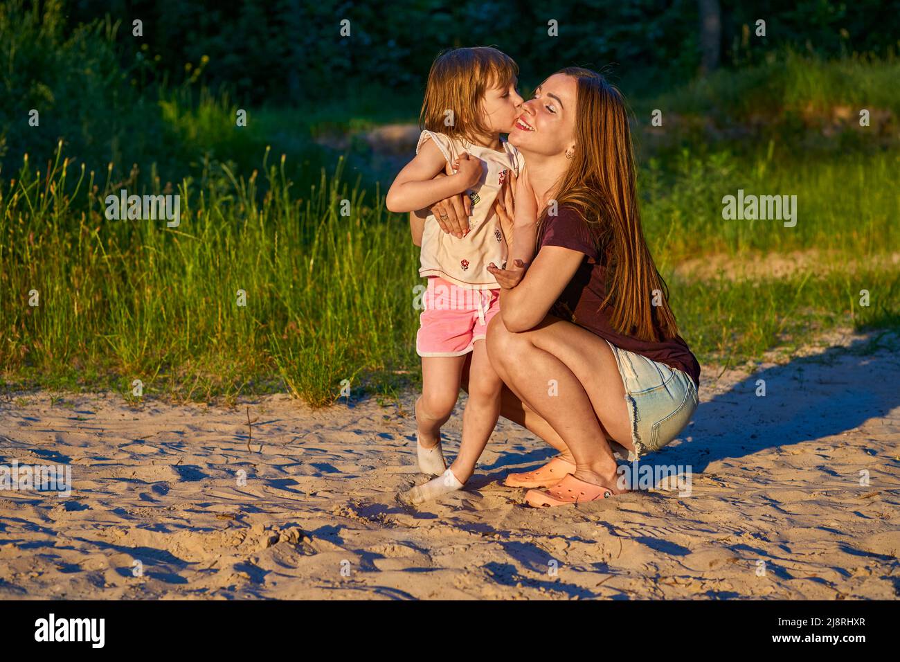 Wonderful cute girl child kissing happy mom among sand dunes and greenery Stock Photo