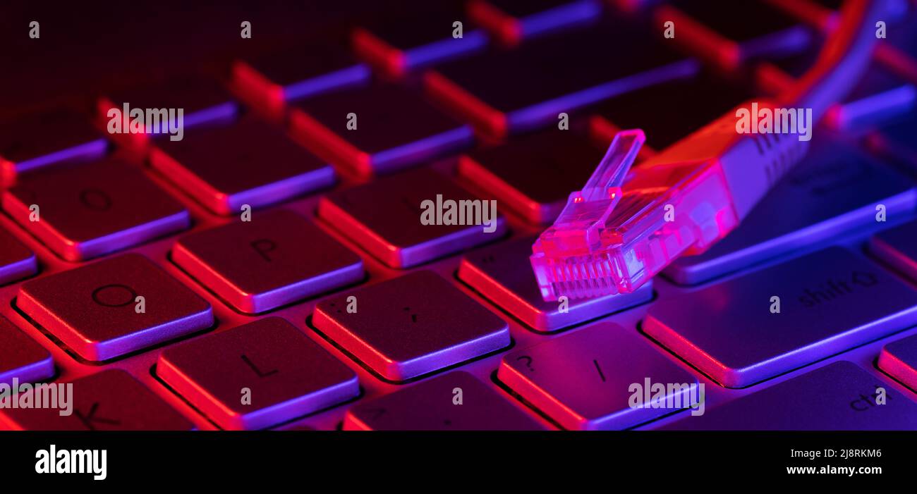 RJ45 internet cable on computer keyboard with neon lights. copy space Stock Photo