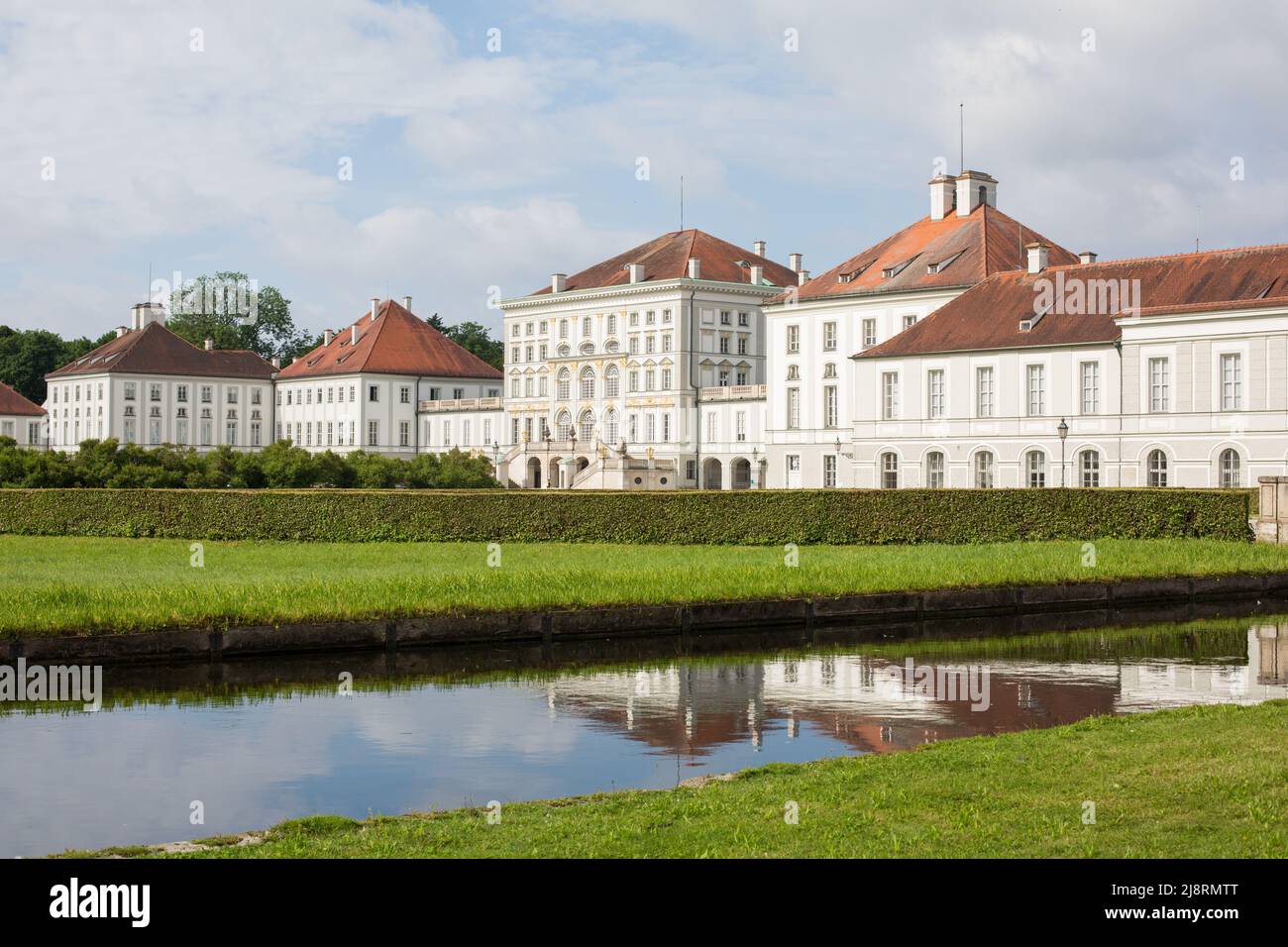 Munich, Germany - Jul 2, 2021: View on the main building of Nymphenburg palace. Meadow and park waters in the foreground. Stock Photo
