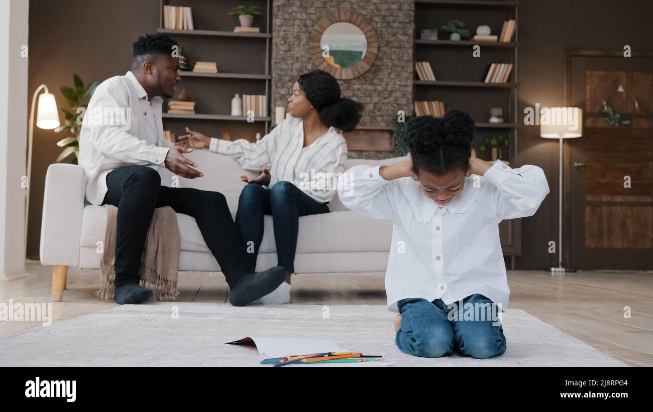 Sad little african daughter child kid girl closing ears upset at parents fighting arguing quarrel conflict at home stressed baby suffer from psycholog Stock Photo