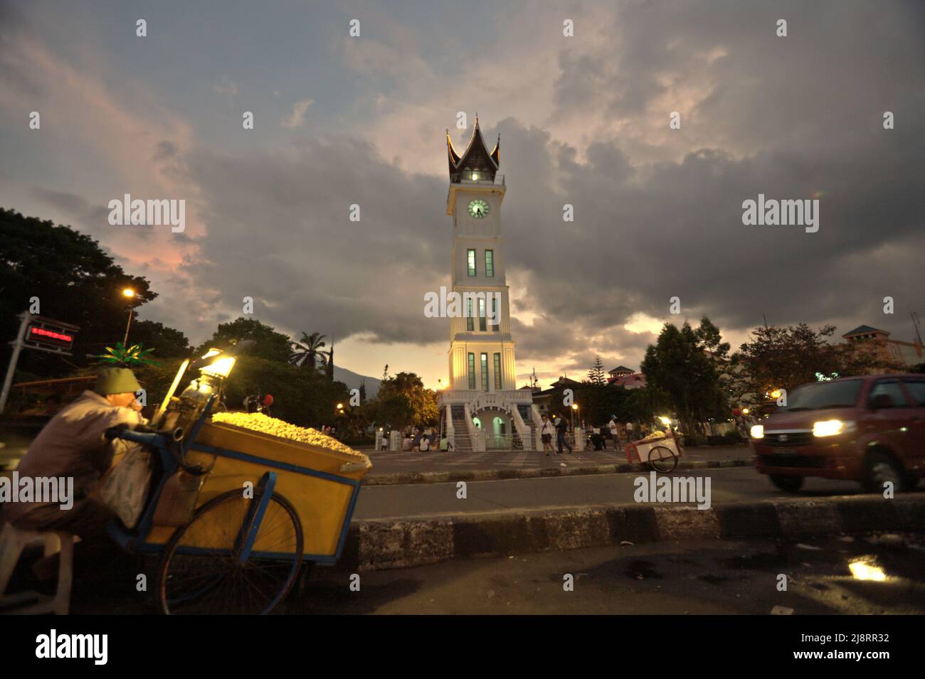 Steamed peanuts vendor and road traffic in a background of big clock tower known locally as Jam Gadang, a major landmark in Bukittinggi, West Sumatra, Indonesia. Stock Photo