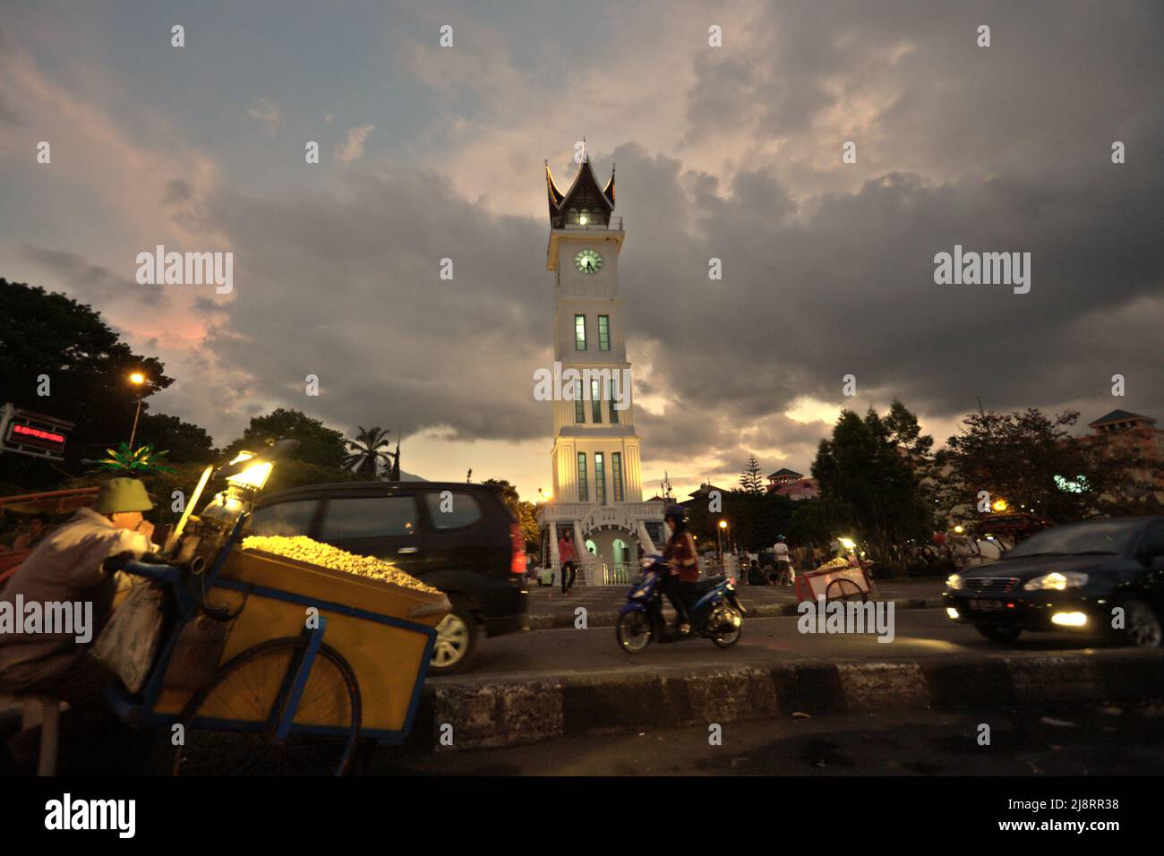 Steamed peanuts vendor and road traffic in a background of big clock tower known locally as Jam Gadang, a major landmark in Bukittinggi, West Sumatra, Indonesia. Stock Photo