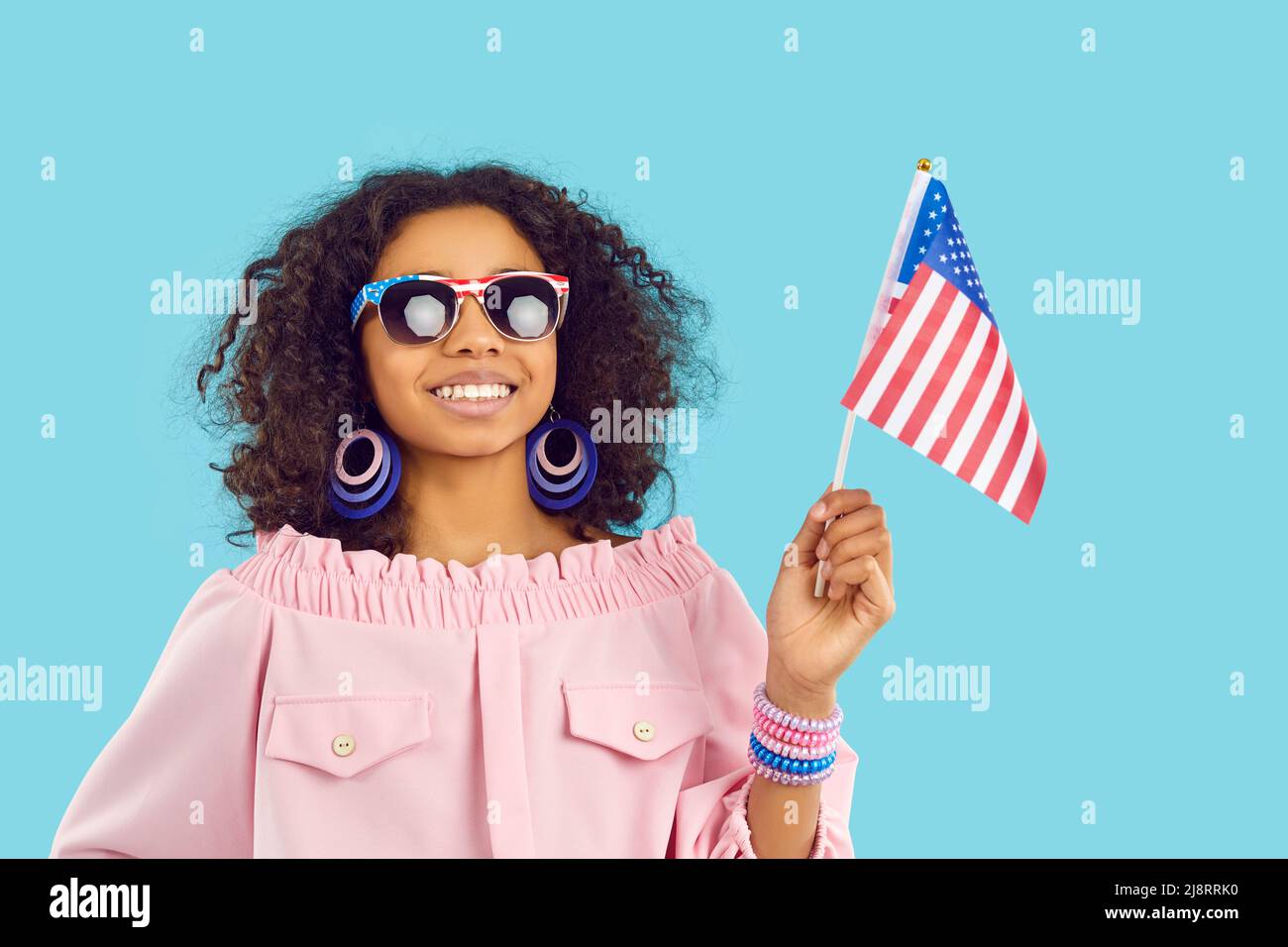 Cute african american preteen girl with national american flag smiling on light blue background. Stock Photo