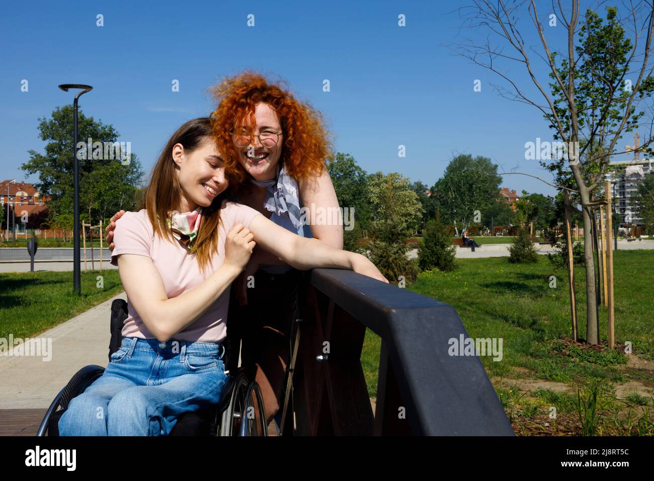 Paraplegic woman and her friend laughing and embracing each other on a sunny summer day Stock Photo