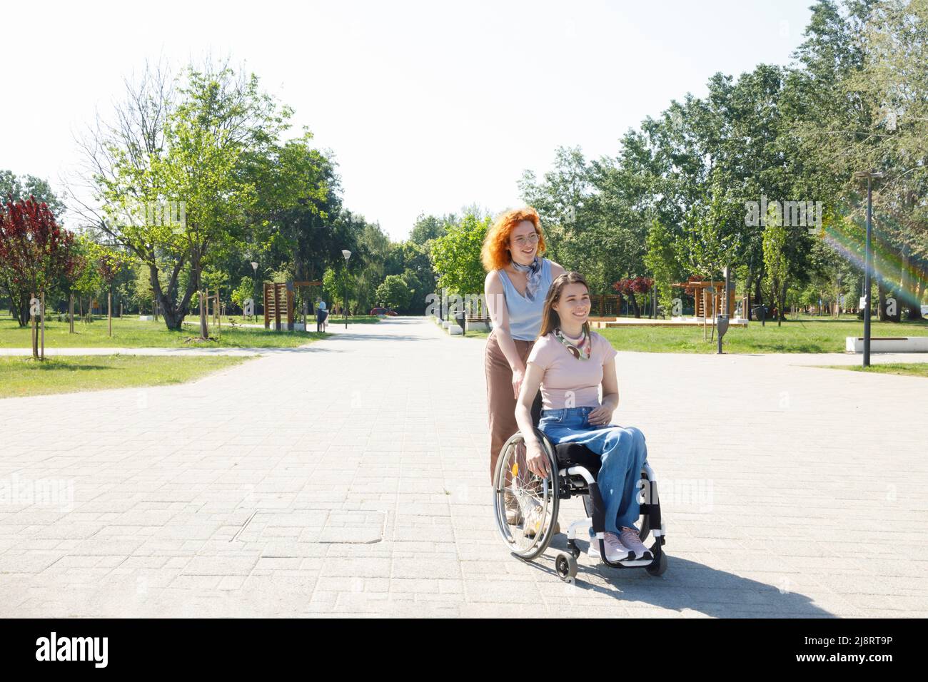 Two diverse female friends strolling through a park on a sunny summer day Stock Photo