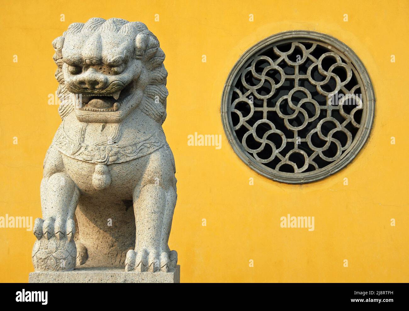 Zhenjiang, Jiangsu Province, China: A traditional Chinese lion statue against a yellow background and circular window at Dinghui Temple in Zhenjiang. Stock Photo