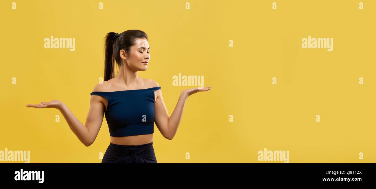 Smiling woman standing on knees, keeping hands palms up indoor. Portrait view of graceful girl in black top kneeling with arms bent at elbows, isolate Stock Photo