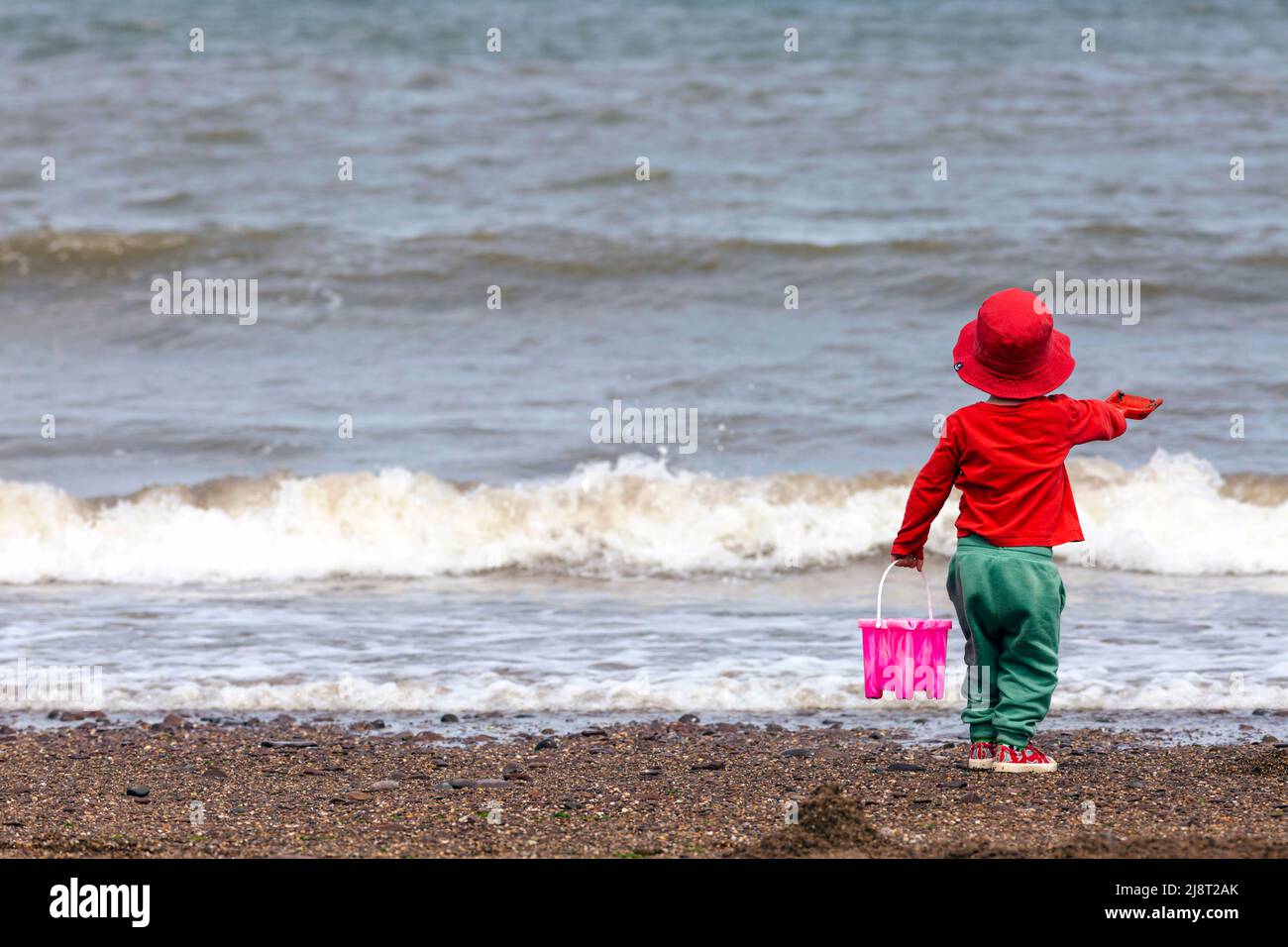 Young boy on a beach, holding a bucket and spade, and looking out to