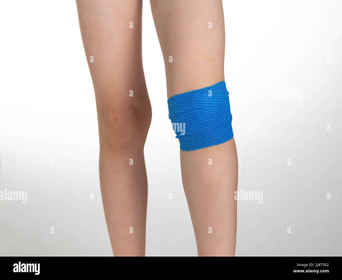 Blue elastic bandage on the knee joint on the child's leg. White