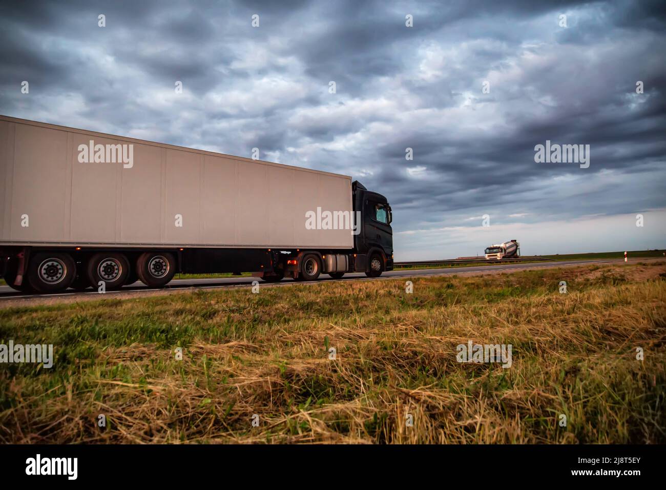 A modern truck with a semitrailer refrigerator transports cargo against the backdrop of a cloudy sky with clouds. Transportations carried out by road Stock Photo