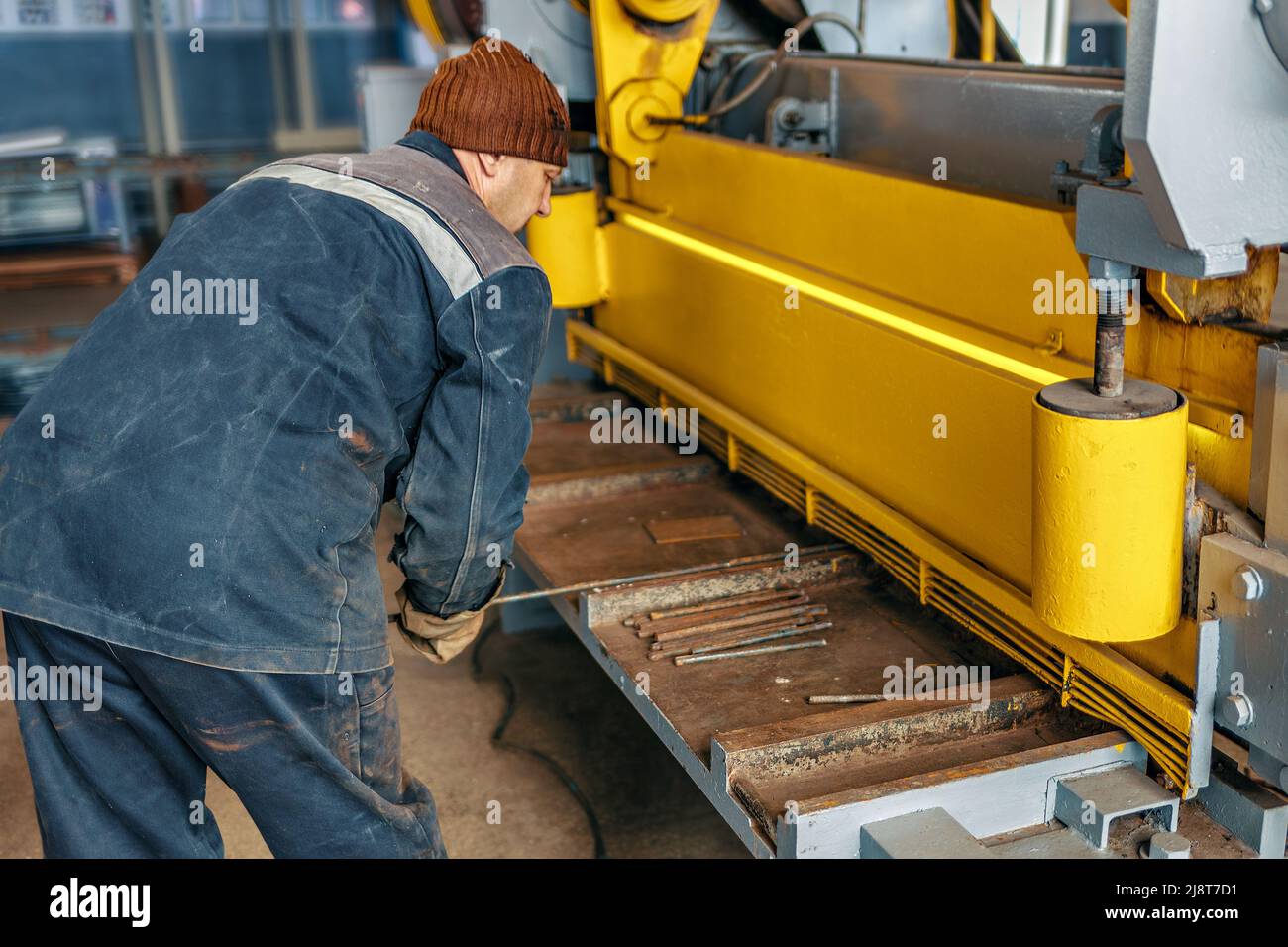 Worker cuts metal on mechanical guillotine machine in production hall. Industrial equipment for metal cutting. Real scene. Real workflow. Man at work. Stock Photo