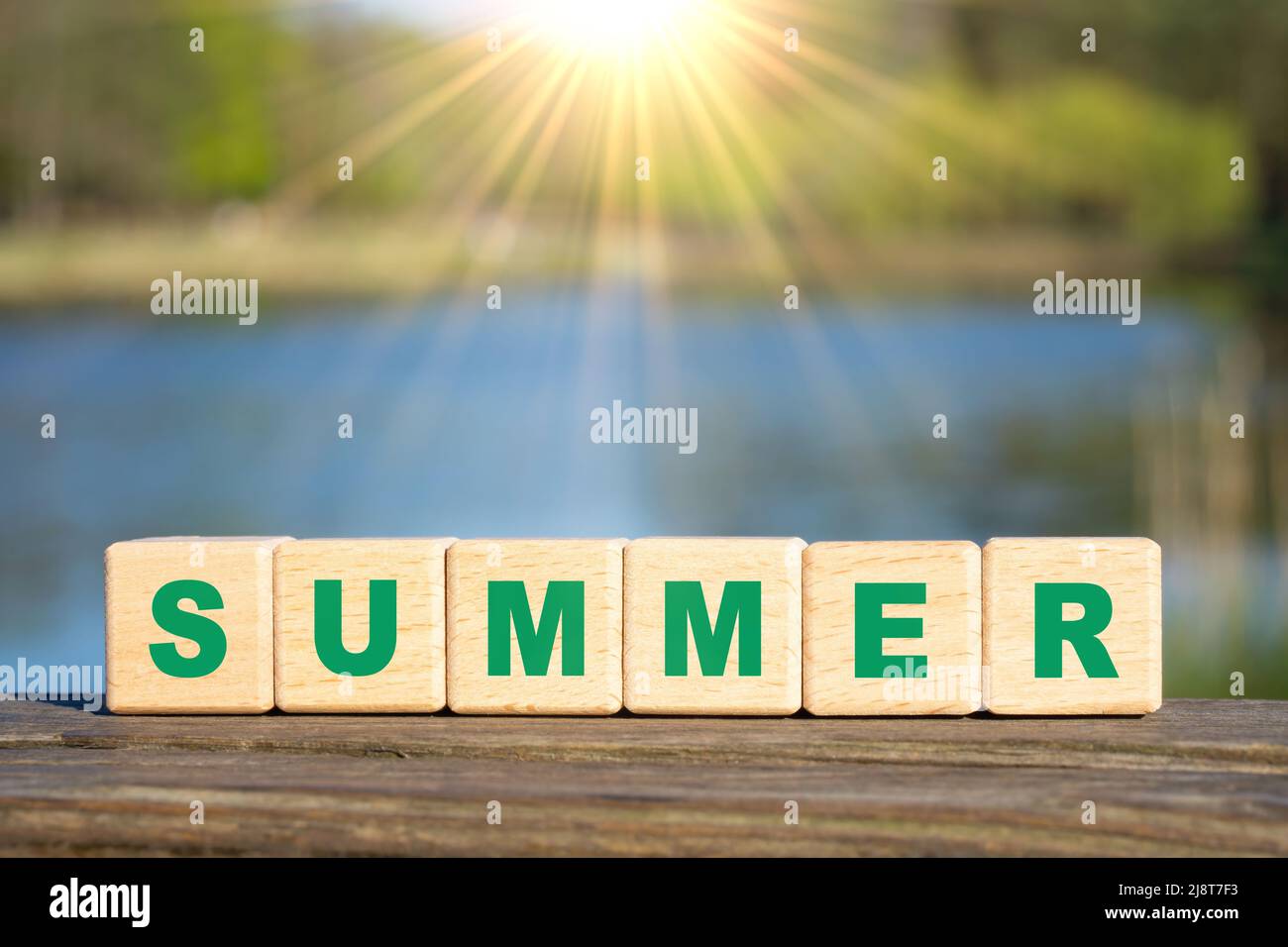 Word SUMMER made from wooden alphabet blocks against a lake background. Summertime vacation concept. Stock Photo