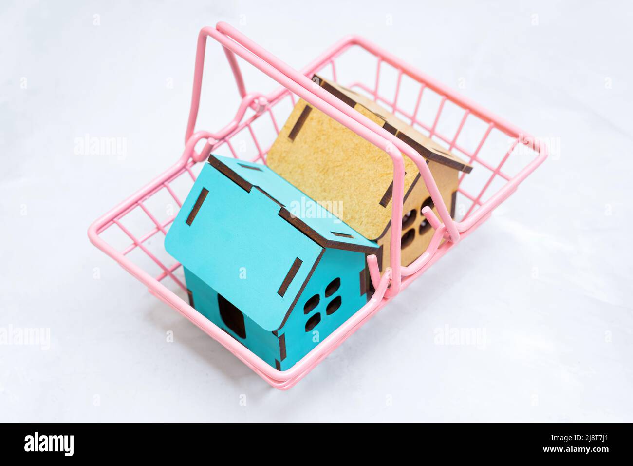 Top view of toy wooden houses in a pink shopping cart on a neutral background. Real estate sale concept. Stock Photo