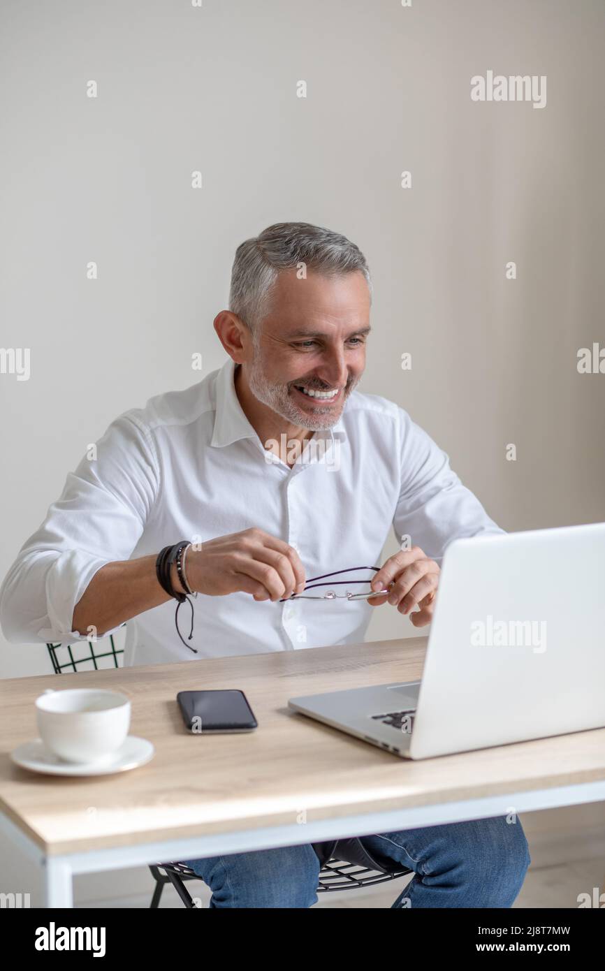 Joyful man holding glasses looking at laptop screen Stock Photo