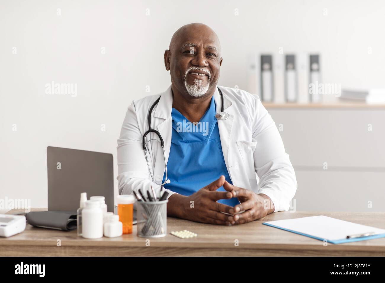 Portrait of smiling doctor looking at camera sitting at desk Stock Photo