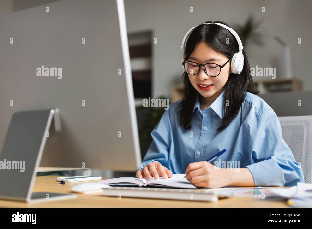 Woman sitting at desk, using computer and writing in notebook Stock ...