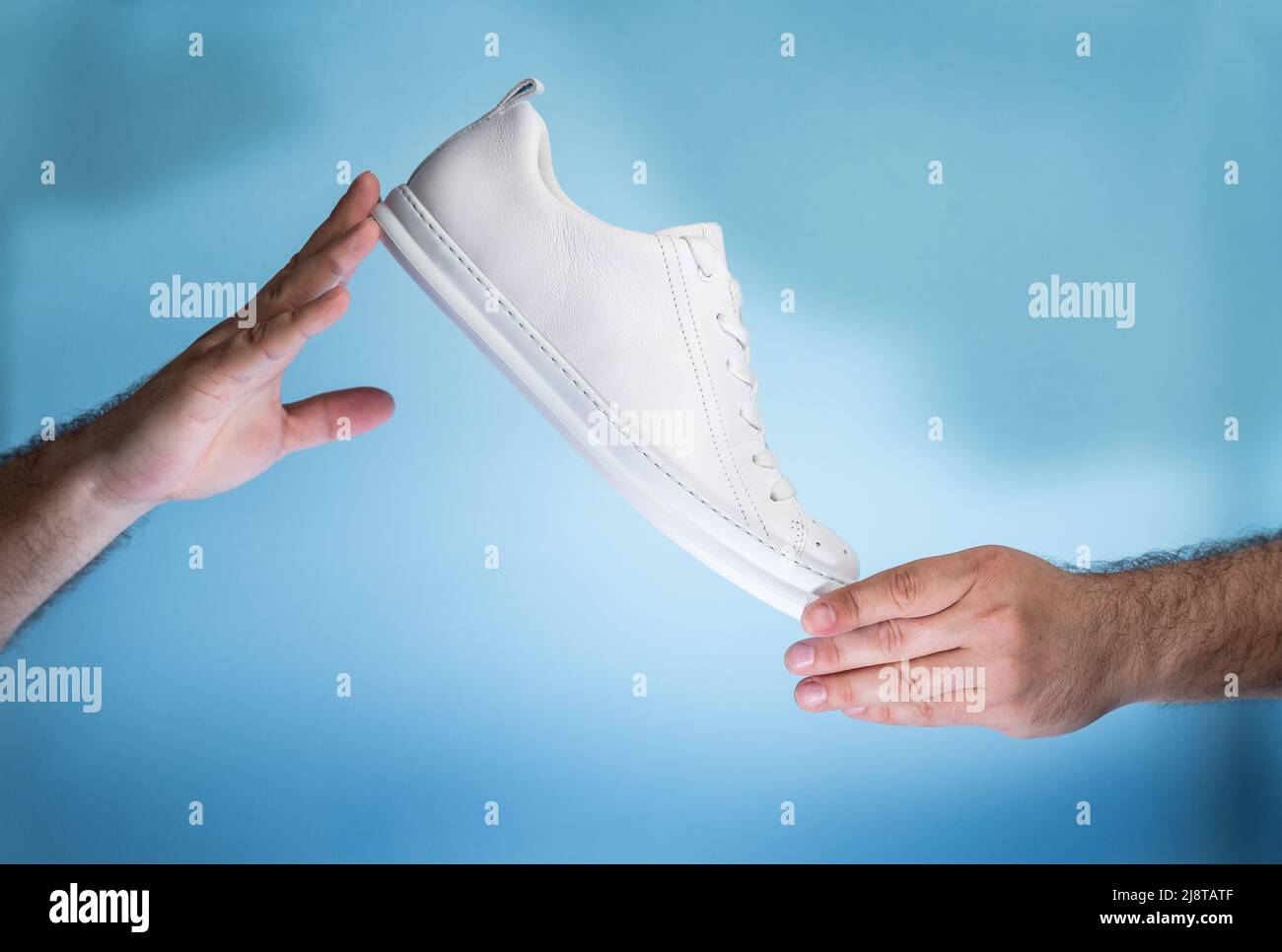 Hands holding New unbranded tennis shoes on blue background. New unbranded Sneakers or trainers - Men's sport footwear. Pair of sport shoes. Stock Photo