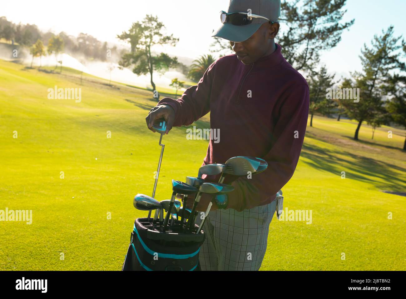 African american young man wearing cap putting golf clubs in bag at