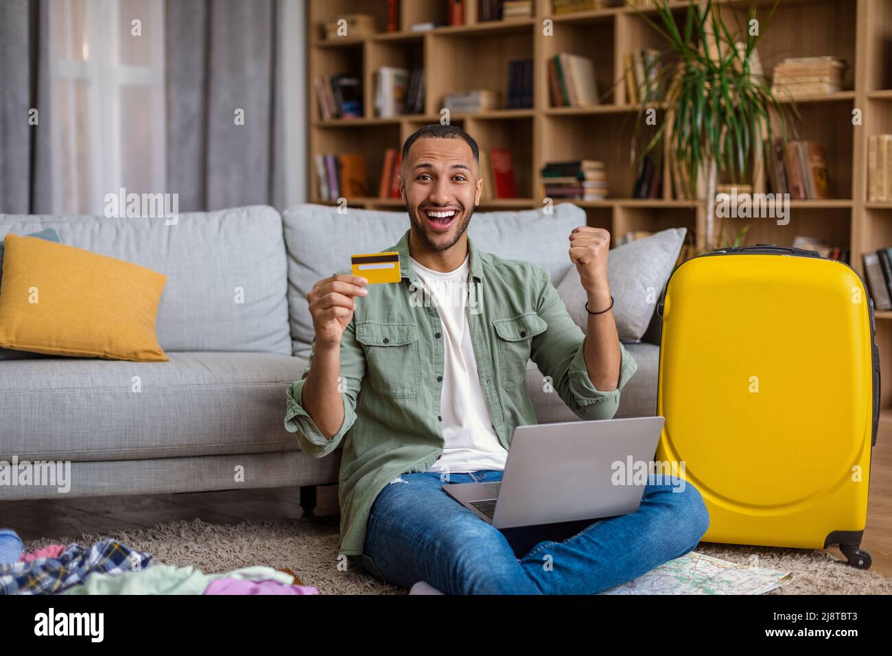 Happy black man using credit card and laptop, booking abroad trip, making hotel reservation on web from home Stock Photo