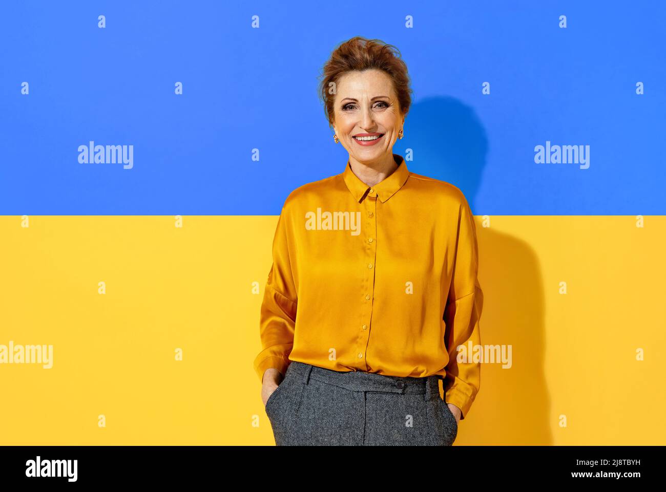 Ukrainian woman laughs happily. Photo of kind attractive woman in yellow shirt against the background of the flag of Ukraine Stock Photo