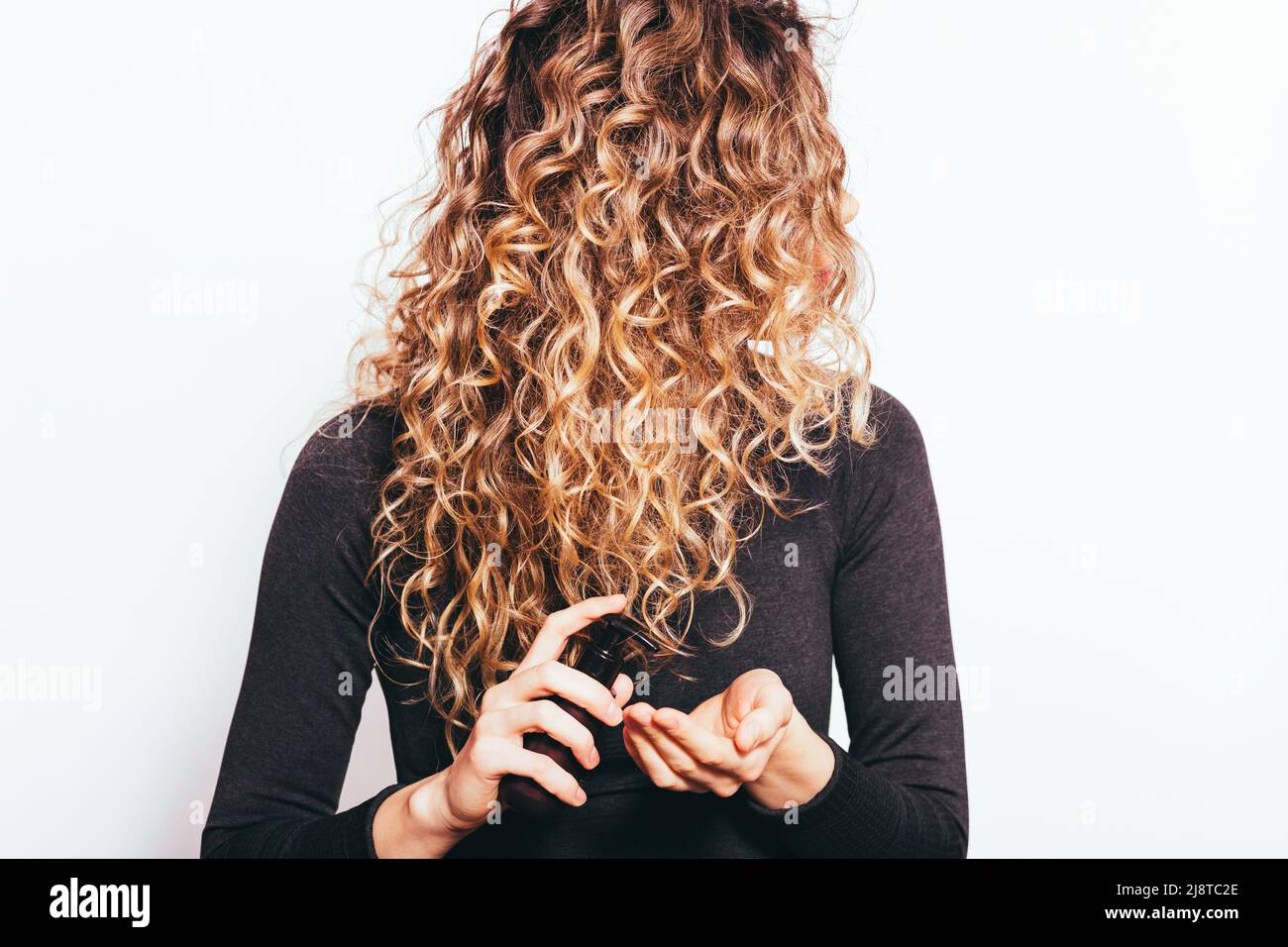 Young woman holding cosmetic oil applying on her curly hair to prevent