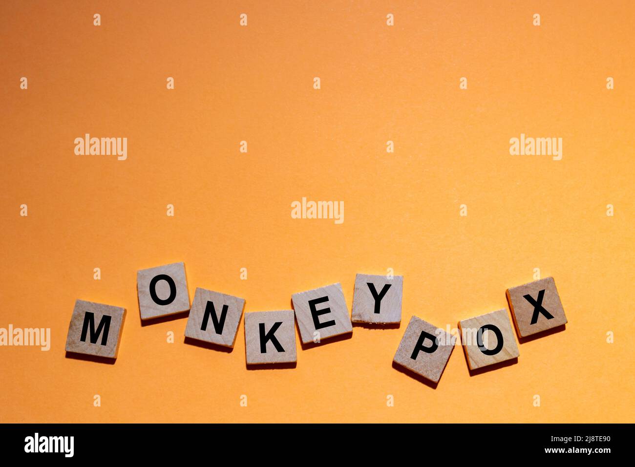 MONKEYPOX. Word written on square wooden tiles with an orange background. Monkeypox is a zoonotic viral disease that can infect nonhuman primates Stock Photo