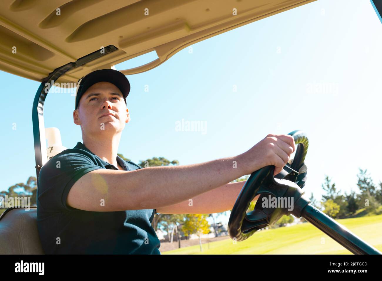 Low angle view of caucasian young man looking away while driving golf cart against clear sky Stock Photo