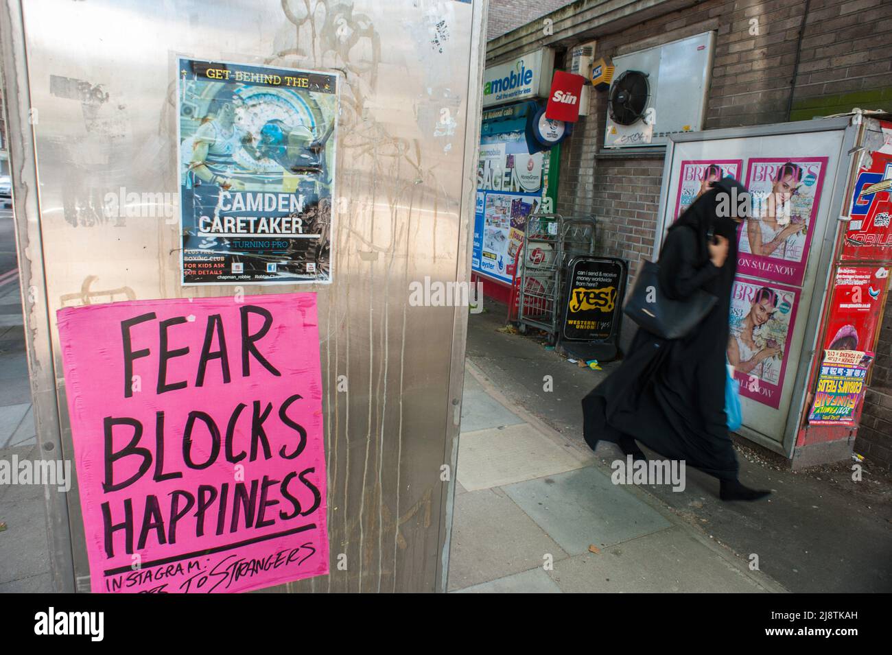 London, 05/08/2017: arab woman passing by a poster 'Fear blocks happiness'. Camden Town. © Andrea Sabbadini Stock Photo