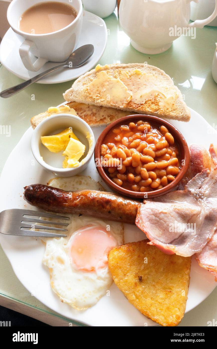 Café meal a small English Breakfast bacon fried egg sausage baked beans hash brown and white bread toast and butter and a cup of tea served in Yorkshi Stock Photo