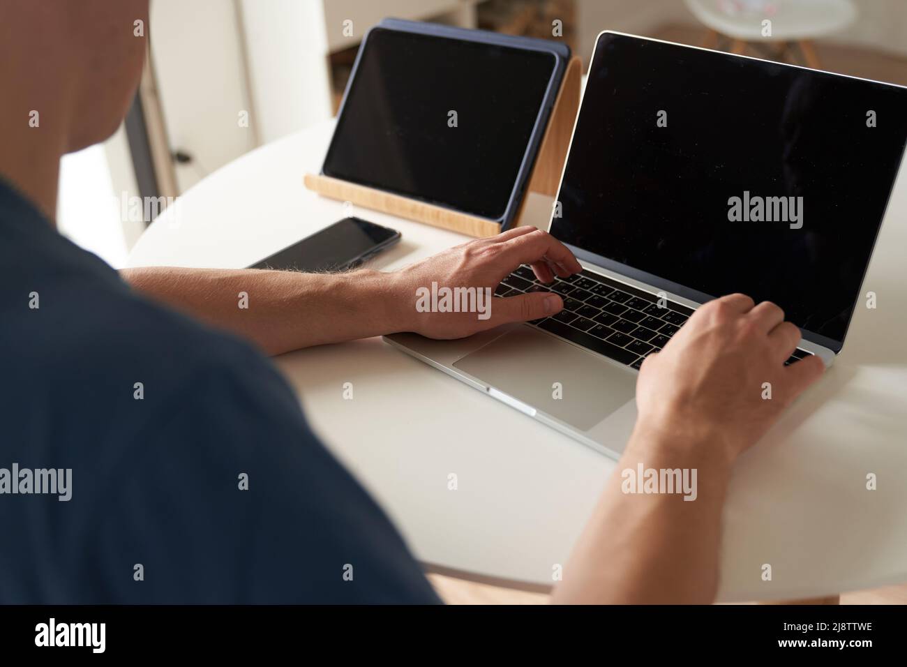 A serious person who works remotely at home. A man enters information into a laptop. Layout concept, design. Black screens on laptops and tablets. Layout for your design. High quality photo Stock Photo