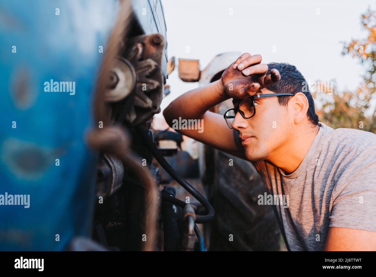 Latin farmer man man passing his stained hand across his forehead and repairing mechanical problems. Stock Photo