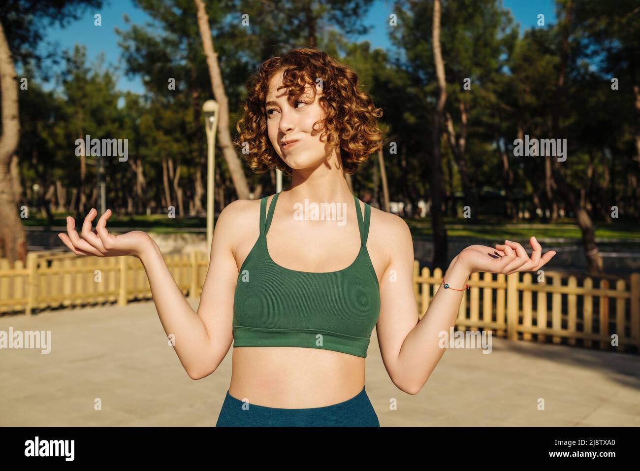 Photo portrait of clueless unsure female shrugging shoulders wearing green sports bra on city park, outdoors. Stock Photo
