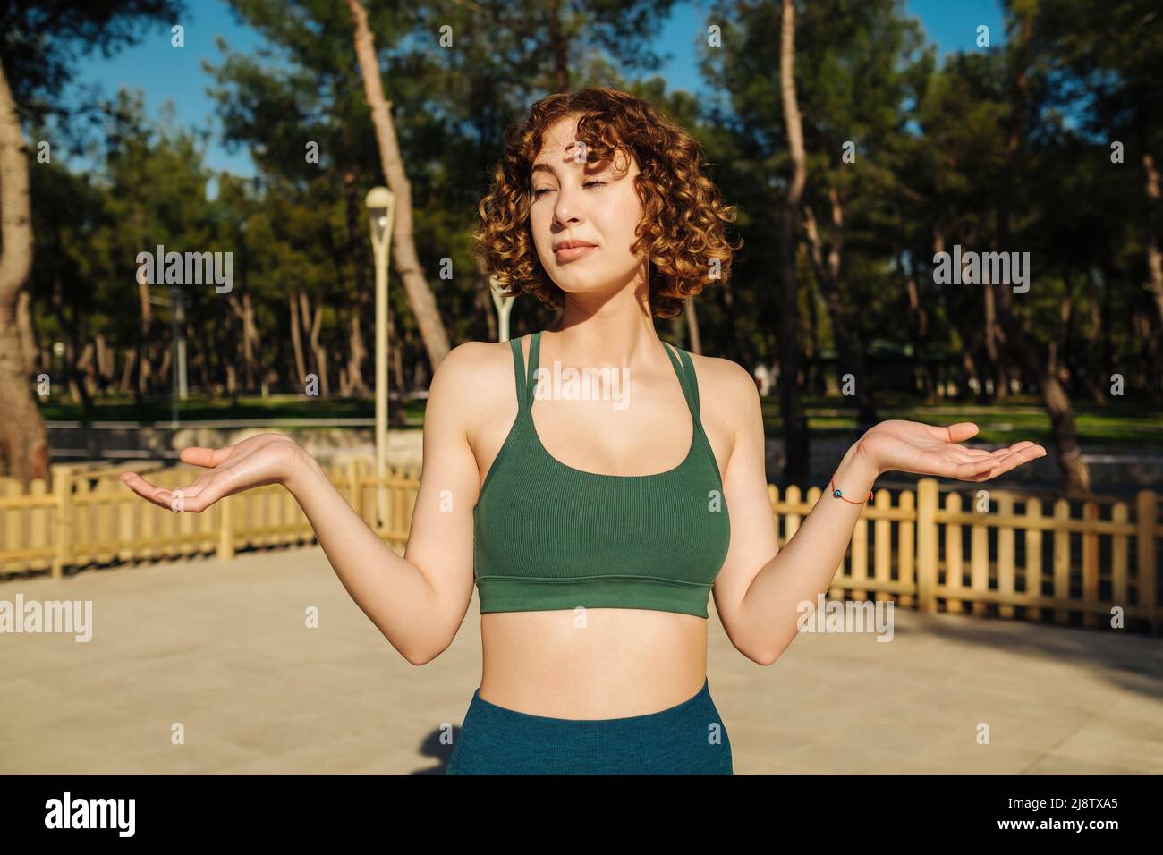 Portrait of a confused young unsure fitness girl shrugging shoulders on a city park, outdoors. Stock Photo