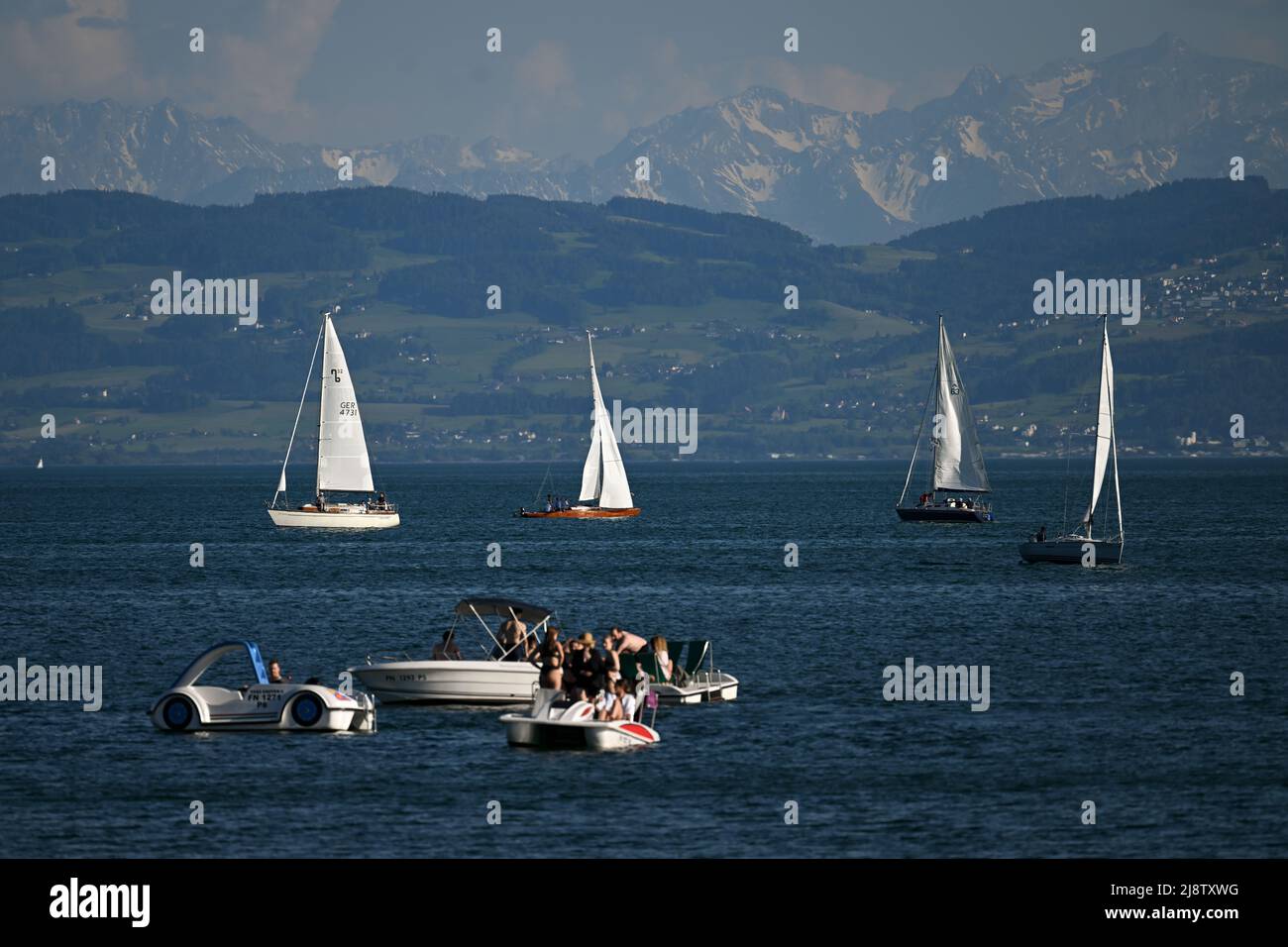Friedrichshafen Am Bodensee, Germany. 18th May, 2022. A regatta is underway  in the evening off Friedrichshafen on Lake Constance, while the Alps in  Switzerland, shrouded in a light haze, can be seen