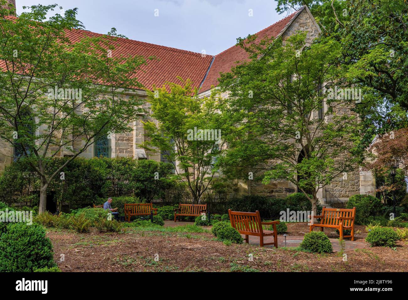 Raleigh, North Carolina, USA - A man read while sitting on a bench in a  peaceful church yard in downtown Raleigh Stock Photo