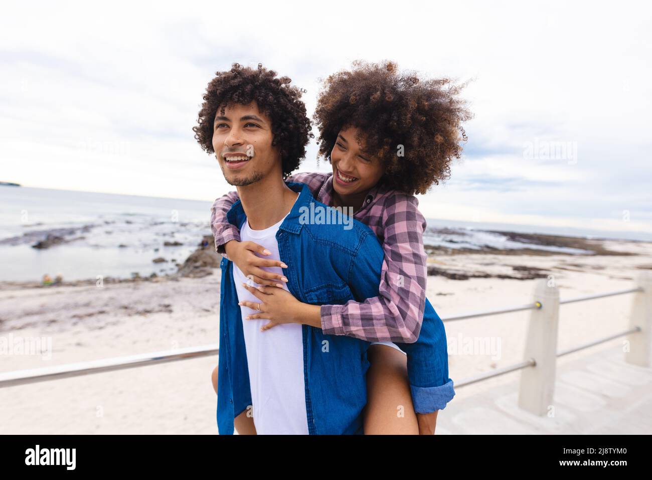 Smiling young man piggybacking afro african american girlfriend by beach, copy space Stock Photo