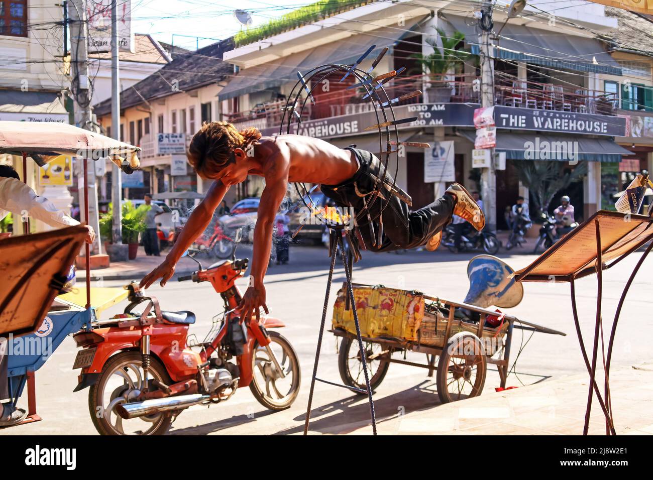 Siem Reap, Cambodia - December 9. 2011: Young khmer cambodian street artist jumping through fire ring hoop with sharp knifes in front of restaurant Stock Photo