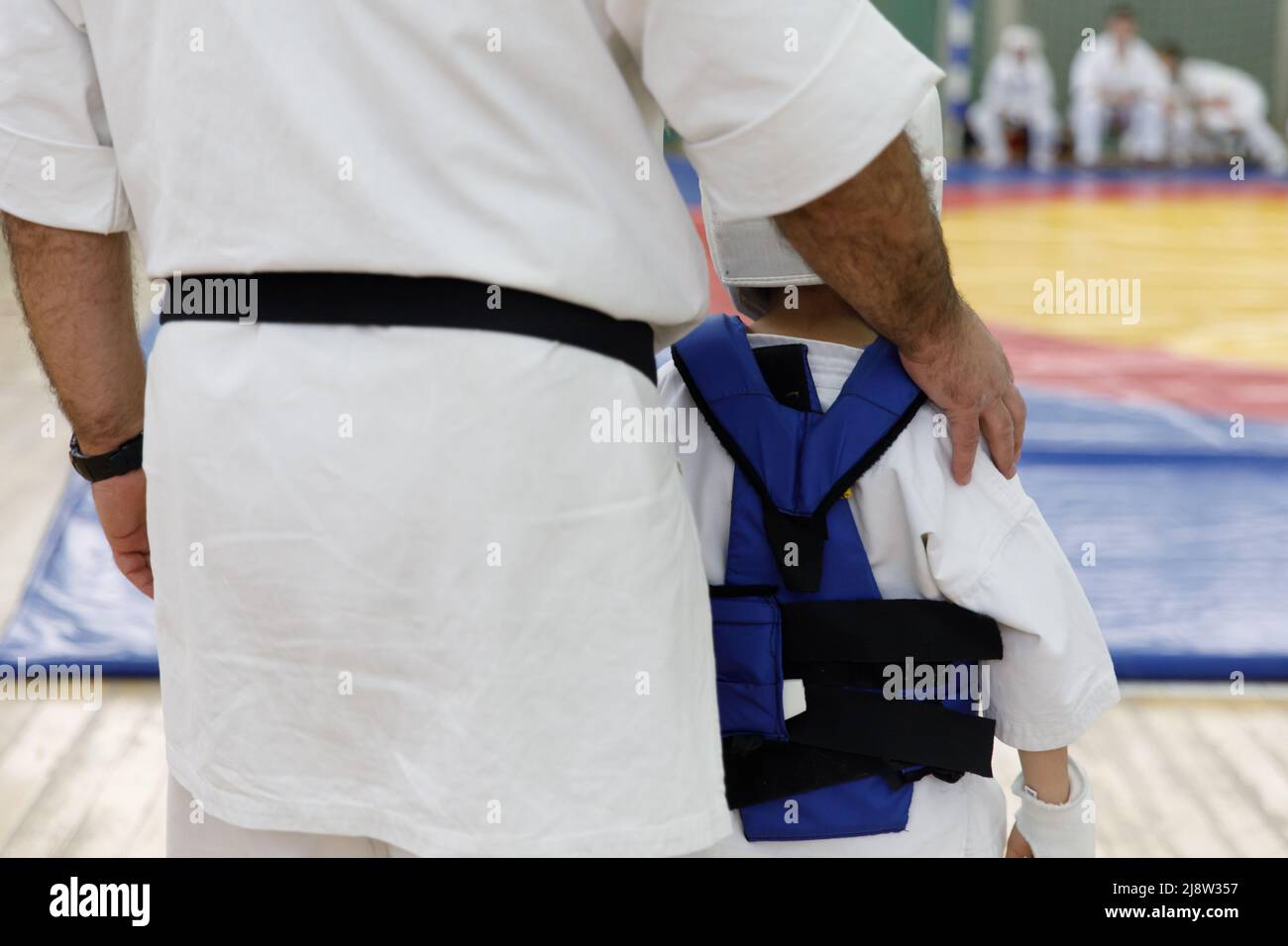 Karate master in a white kimono and with a black belt, stands in front of the formation of his students. Martial arts school in training in the gym Stock Photo