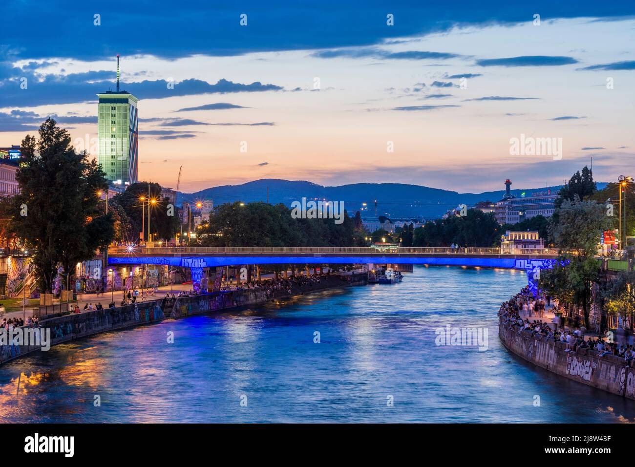 Wien, Vienna: river Donaukanal (Danube Canal), people sit on bank reinforcement, outdoor restaurants and bars, Ringturm high-rise in 01. Old Town, Wie Stock Photo