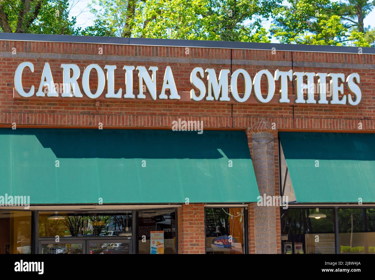 'Carolina Smoothies' exterior facade brand and logo signage on a bright sunny day above green awnings and windows with shadows and green trees. Stock Photo