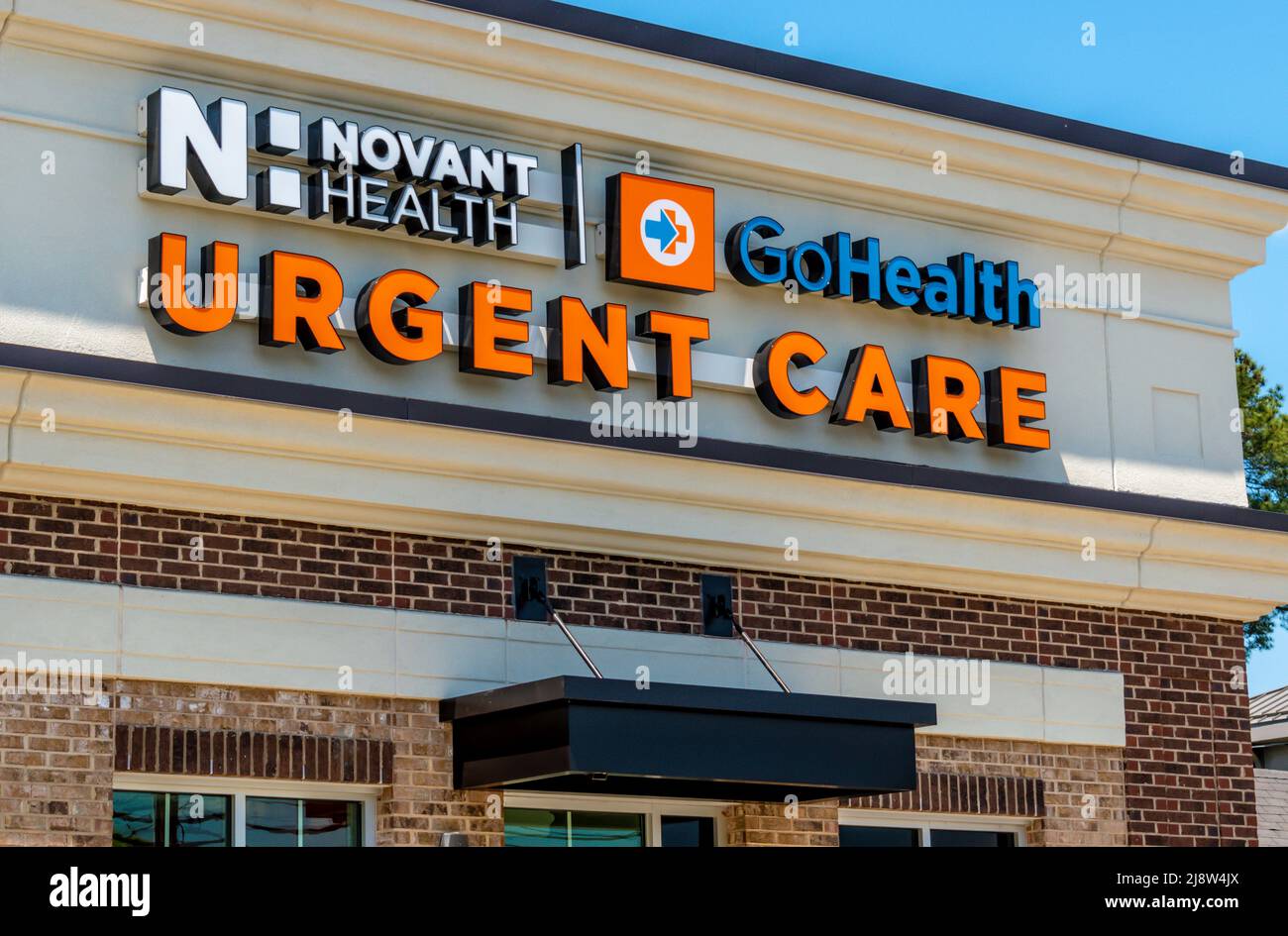 Outdoor facade brand and logo signage for 'Novant Health' Urgent Care medical facility in orange, blue and white letters on a bright sunny day. Stock Photo
