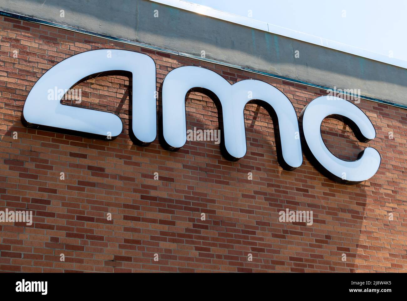 'AMC' movie theater's exterior facade brand and logo signage in white letters on a sunny day with shadows and sky. Stock Photo