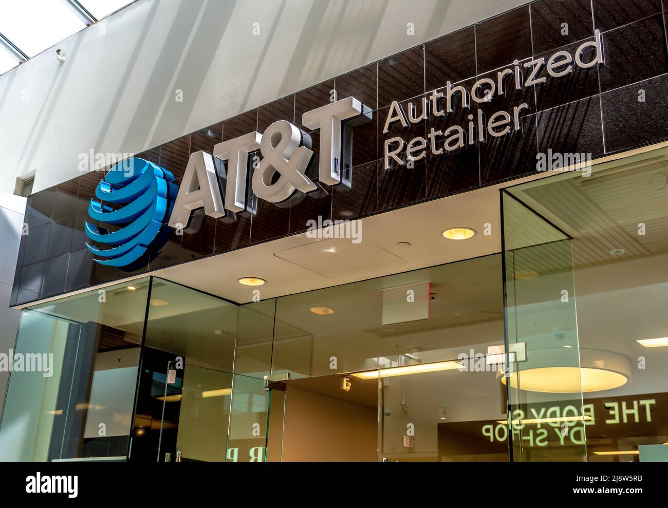 Interior shopping mall 'A T & T' telecom's brand and logo facade signage above glass windows and glass doors with reflections and indoor light. Stock Photo