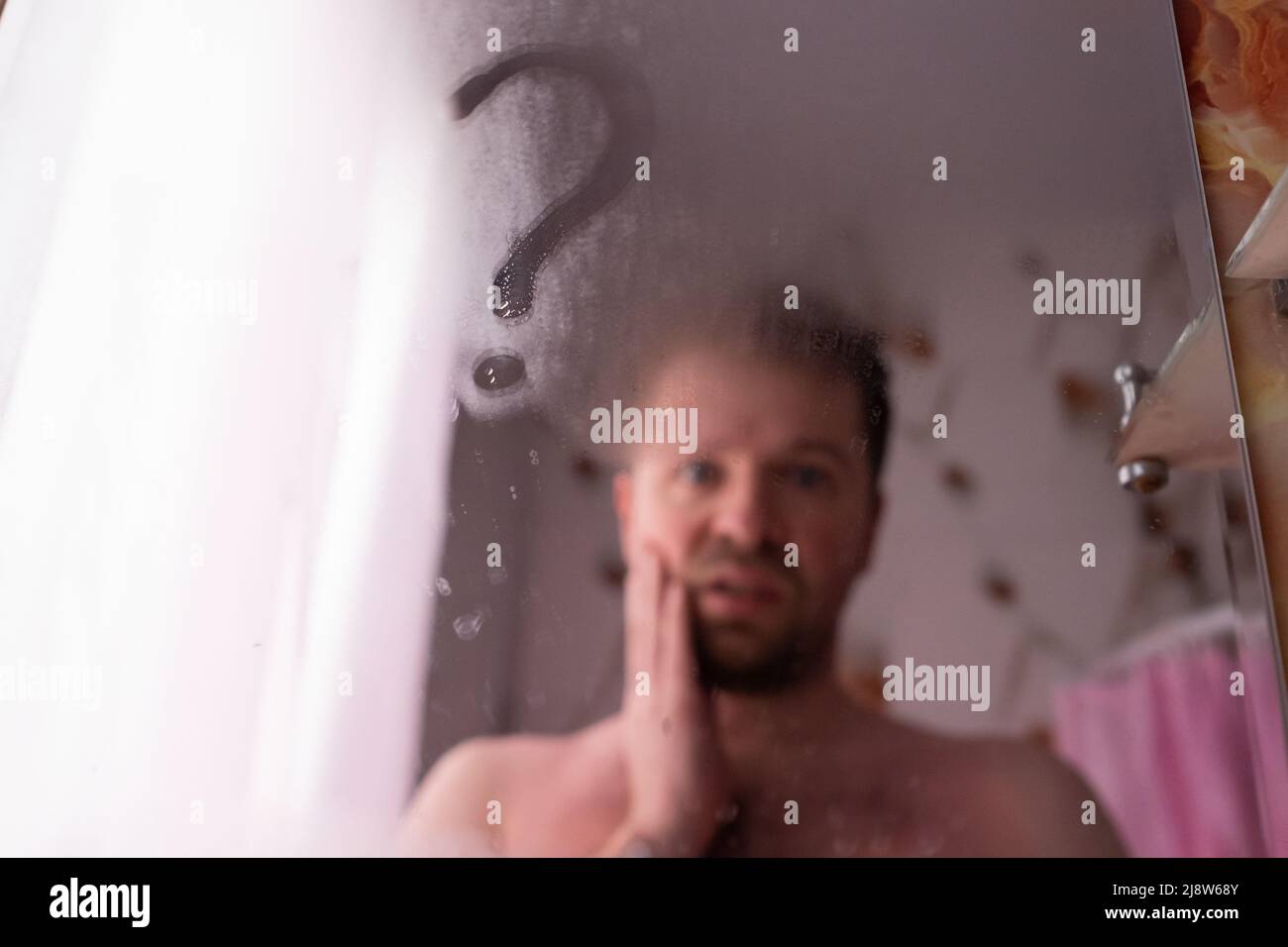 handsome caucasian man looking on his reflection at mirror being puzzled. Sign question drawn on steam Stock Photo