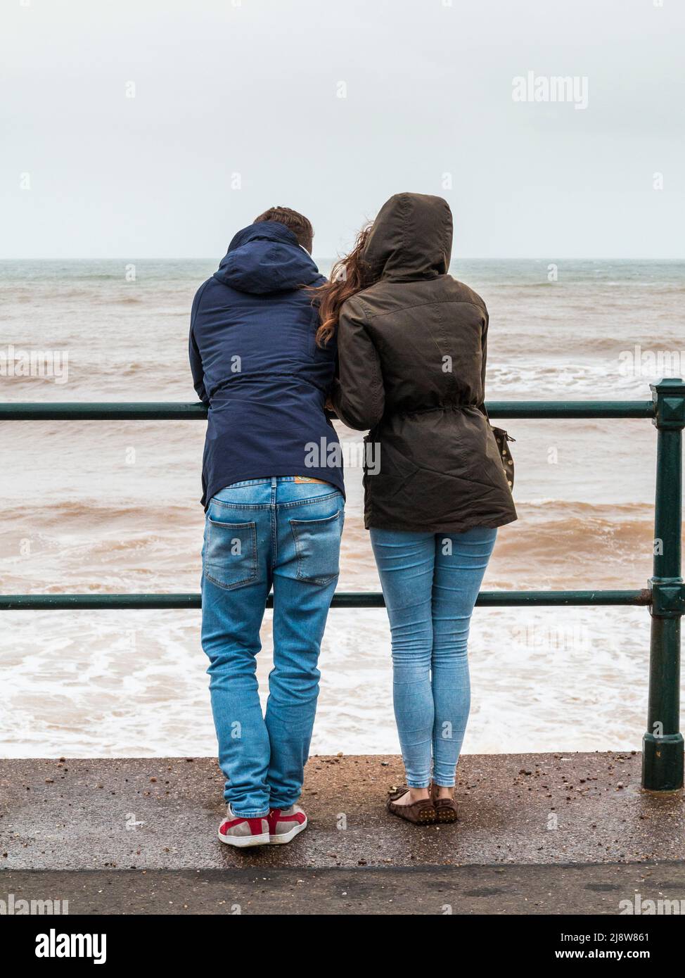 Two people watch the waves during a storm at Sidmouth Devon Stock Photo