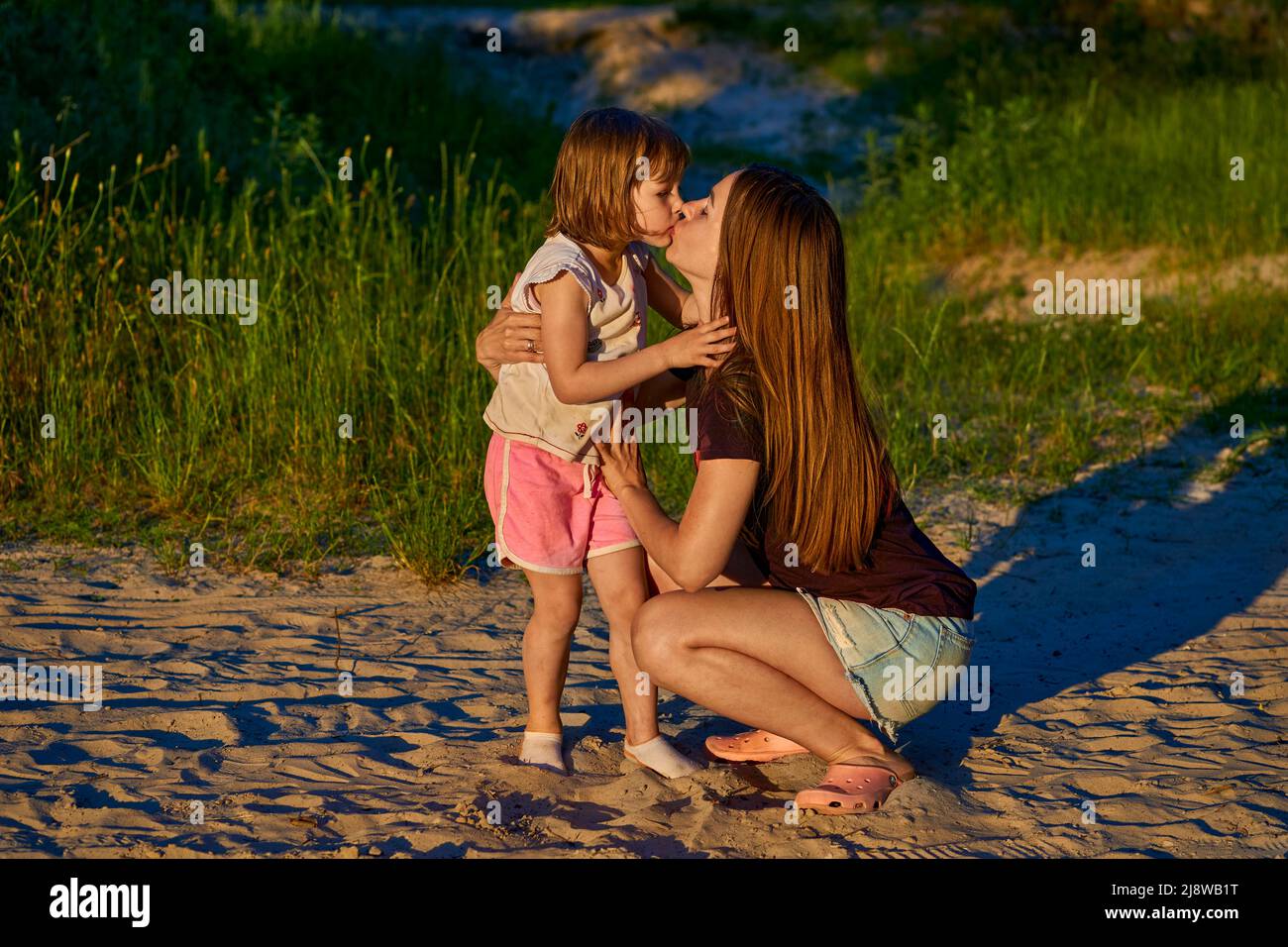 Wonderful cute girl child kissing happy mom among sand dunes and greenery Stock Photo